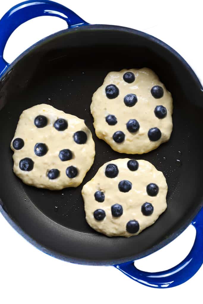 blueberries added to the pancake batter in the pan