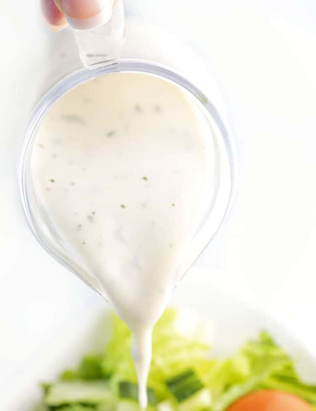 Garlic Dressing being poured onto a green salad.