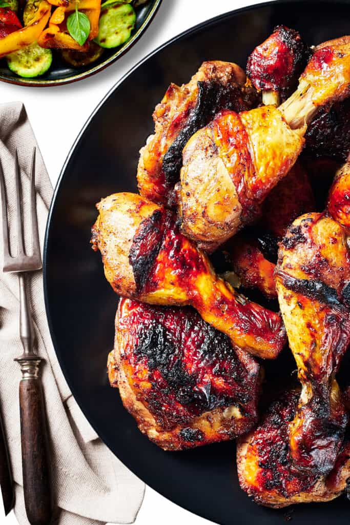 Grilled Chicken Thighs & Legs on a serving dish with a salad and serving fork in the background.