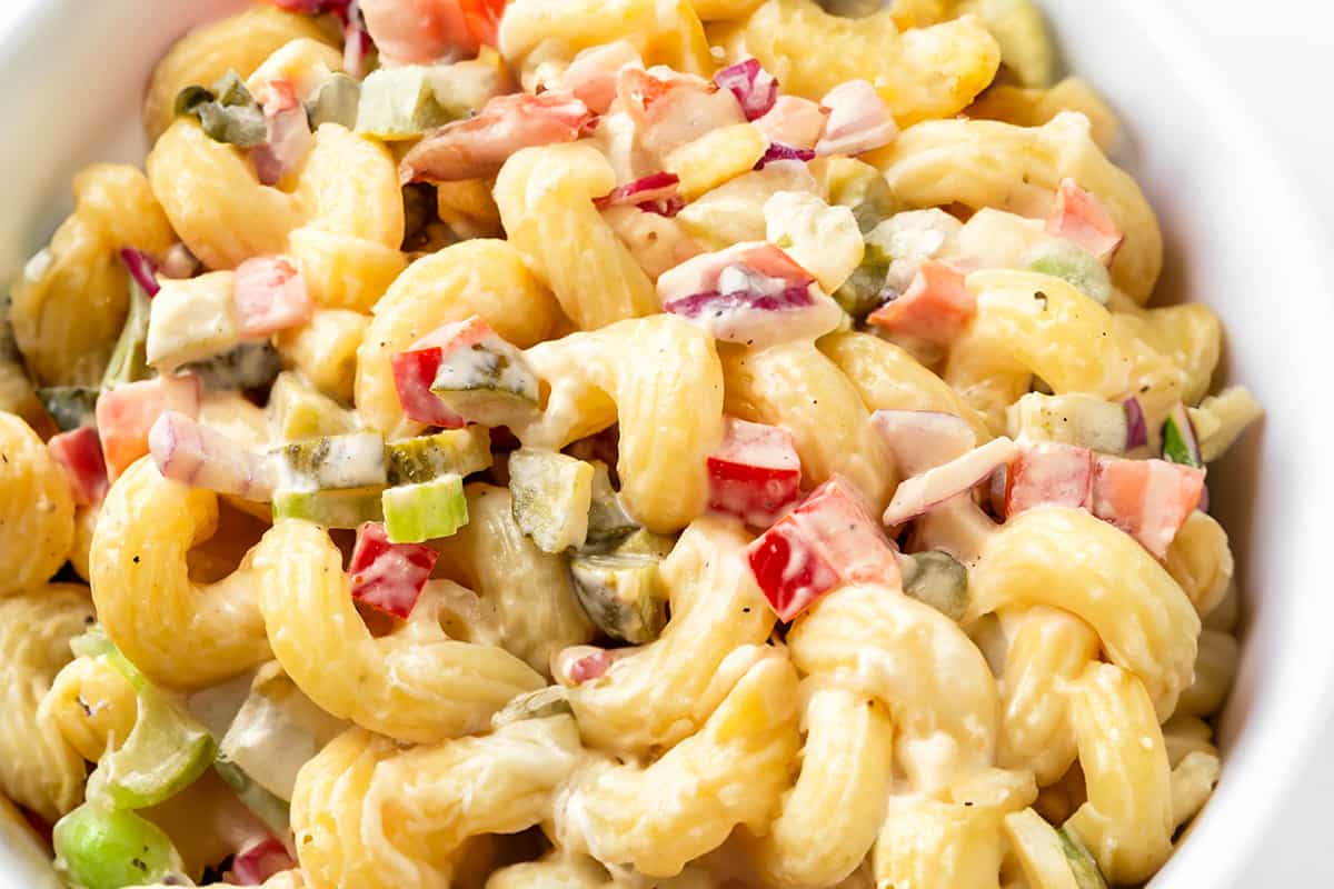 a close up image of a bowl of Amish Macaroni Salad with creamy sauce and chopped vegetables