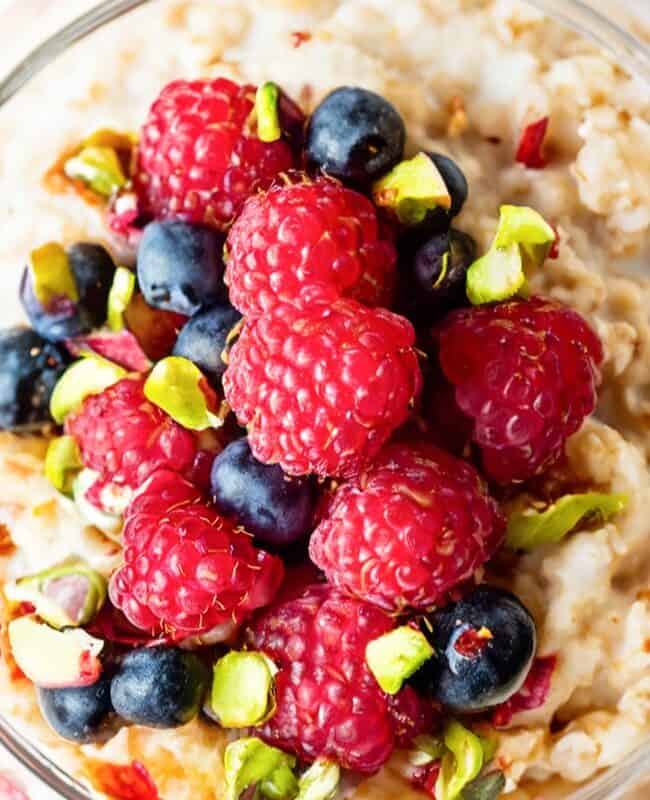 a close up image of a jar filled with overnight oatmeal and topped with mixed berries and chopped pistachios