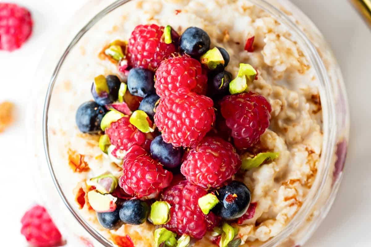 a close up image of a jar filled with overnight oatmeal and topped with mixed berries and chopped pistachios