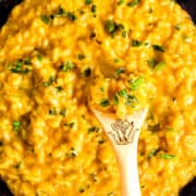 a close up image of The cooked Saffron Risotto in a black pan with a wooden spoon