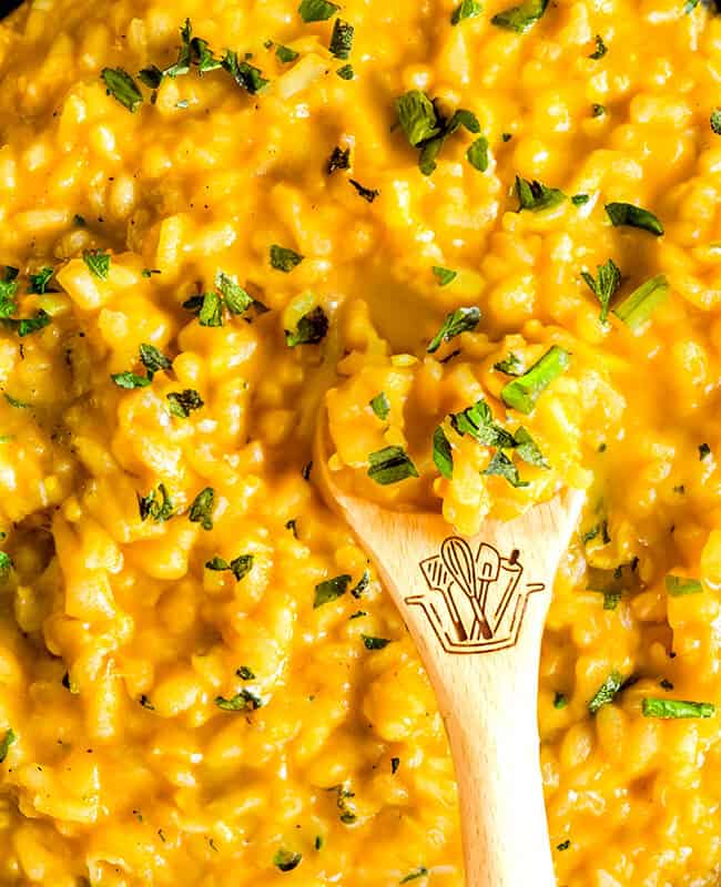 a close up image of The cooked Saffron Risotto in a black pan with a wooden spoon