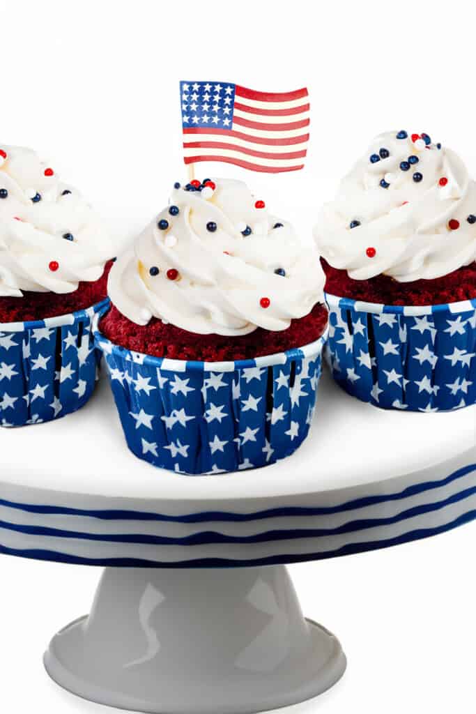 a cake stand with three 4th of July Cupcakes displayed with a mini Americana flag