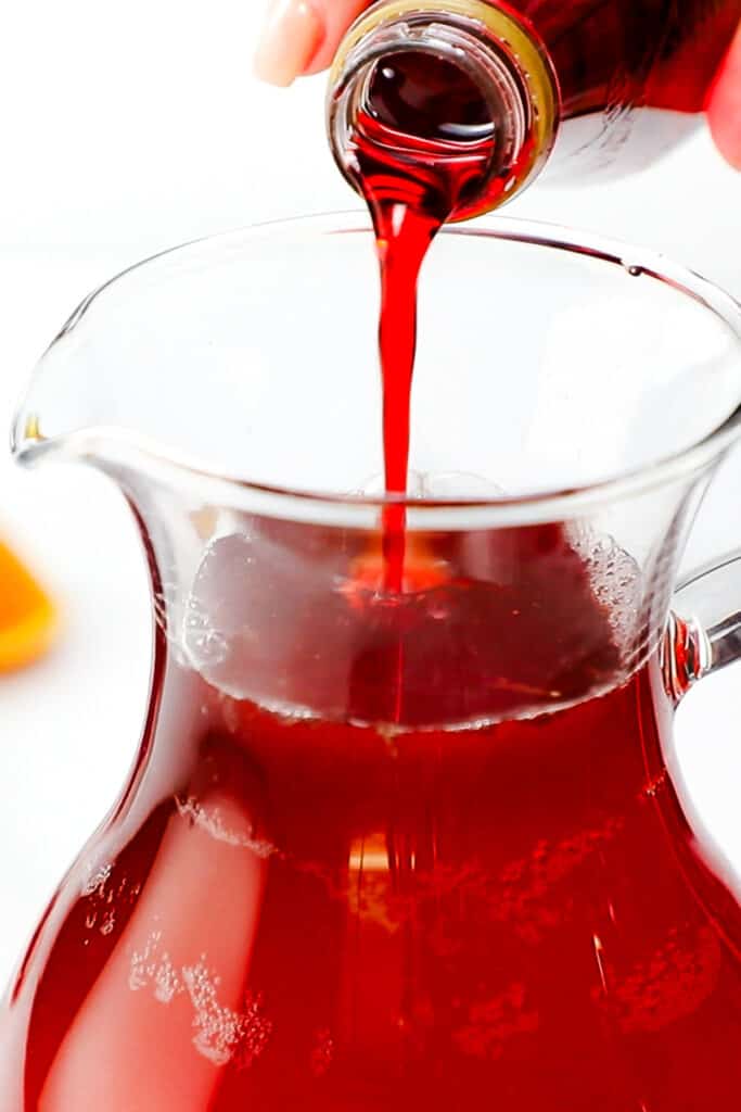 the grenadine being poured into the jug of Rosé Sangria