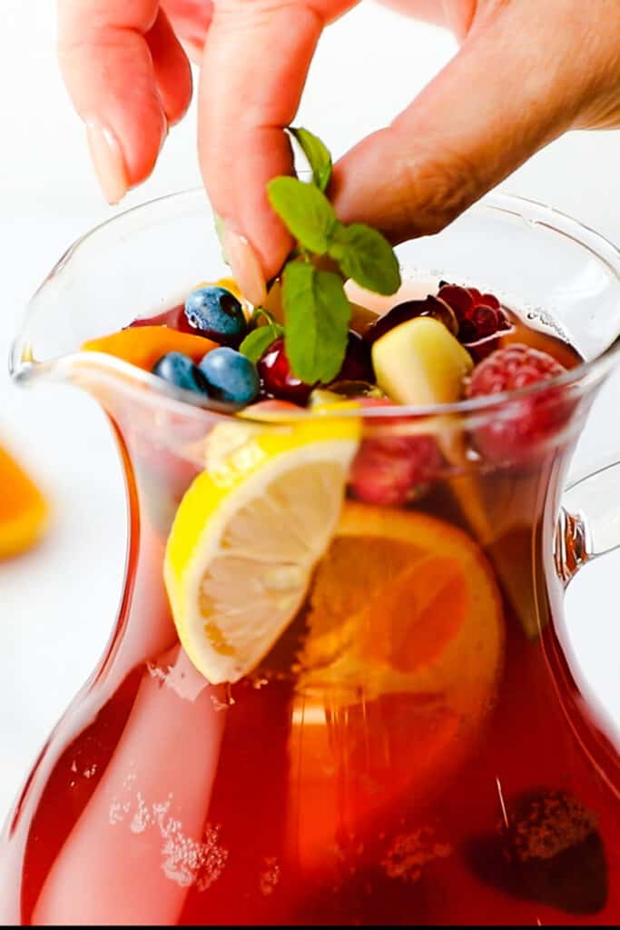 a hand adding fresh mint to a jug of Rosé Sangria.