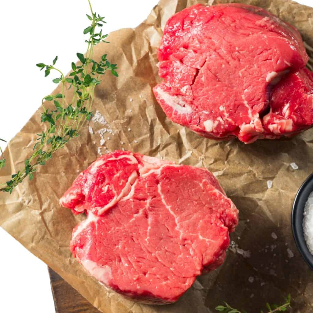 two raw filet mignon steaks on butcher paper with some thyme.