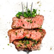 a serving fork with three strips of thick cut grilled filet mignon garnished with parsley.