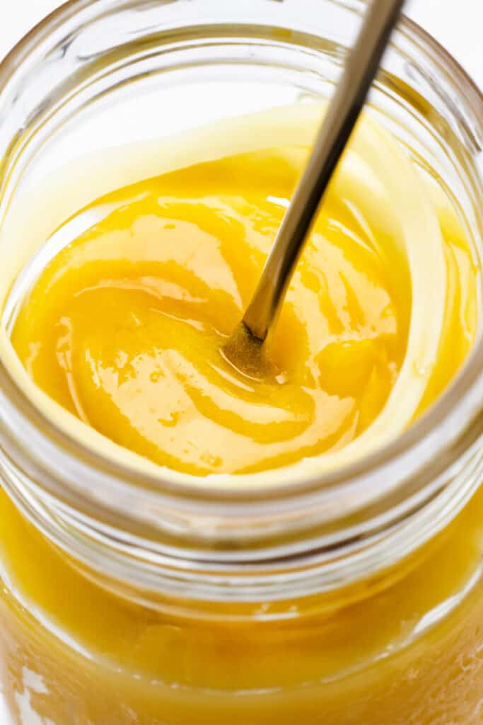 a close up of a jar full of lemon curd with a spoon sticking out of the jar.