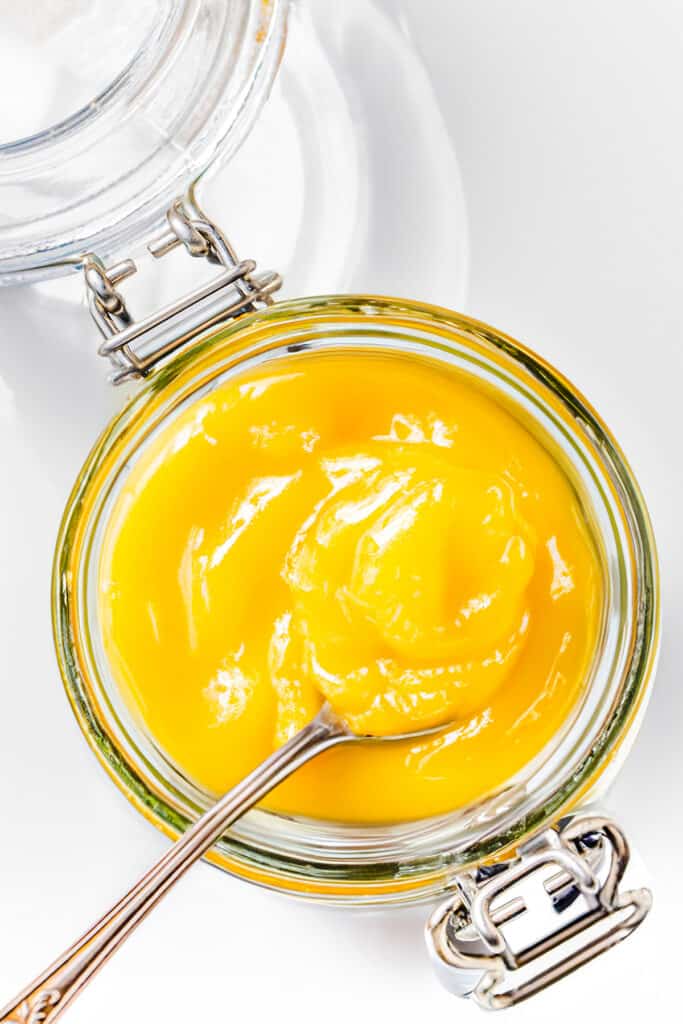 a close up image of an overhead view of a mason jar filled with lemon curd and a spoon in the jar.