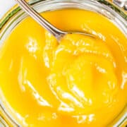 a close up image of an overhead view of a mason jar filled with lemon curd and a spoon in the jar.