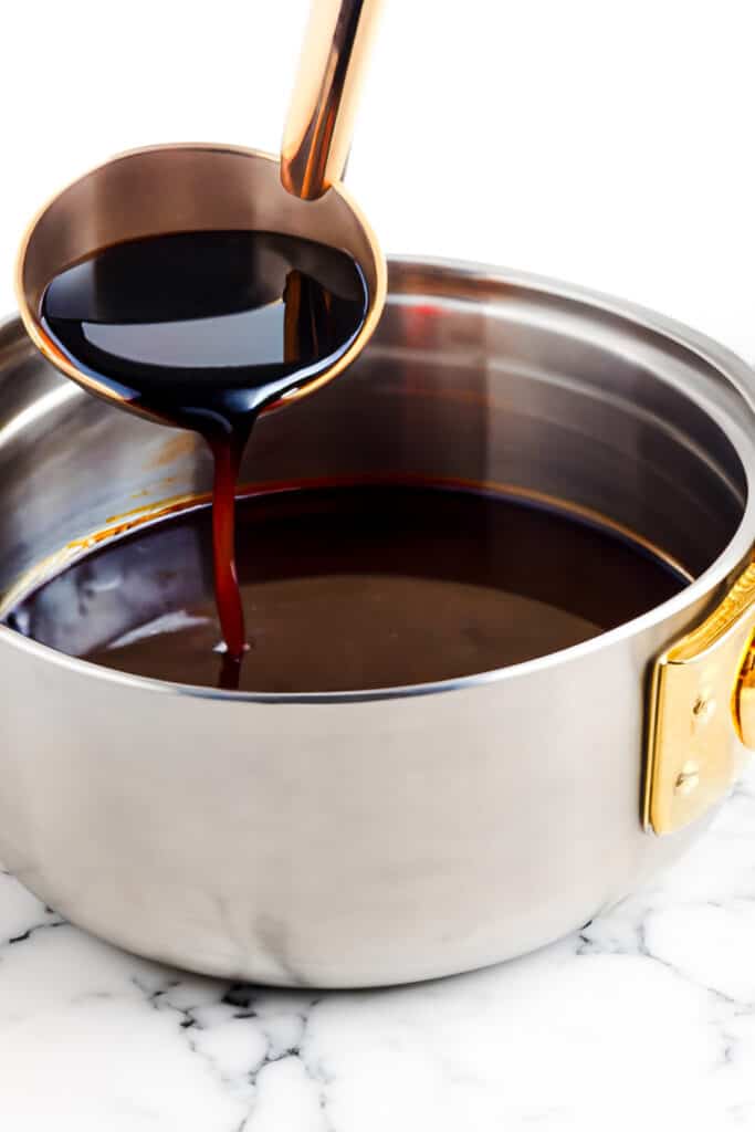 A ladle pouring red wine sauce into a saucepan.