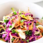 a bowl of vinegar coleslaw with the serving bowl in the background with a spoon.