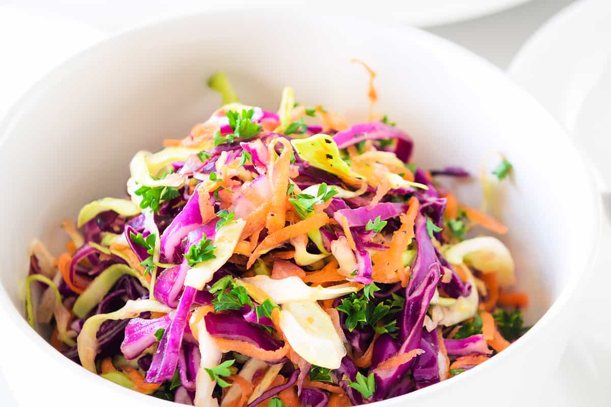 a bowl of vinegar coleslaw with the serving bowl in the background with a spoon.