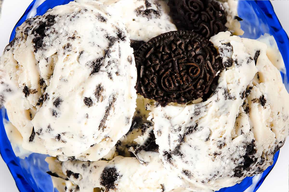 a close up image of a blue glass dessert bowl with scoops of cookies and cream ice cream garnished with broken cookies.