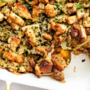 a close up image of a pan of sausage stuffing with a gold spoon in the pan.