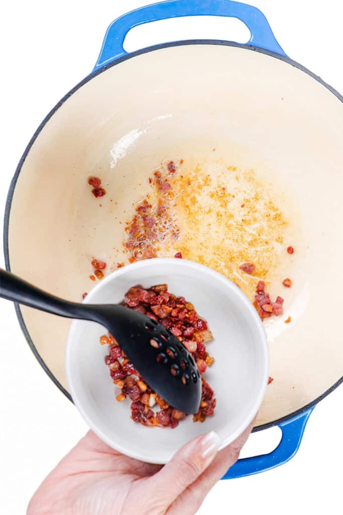 a slotted spoon removing the cooked pancetta from the pan into a bowl.