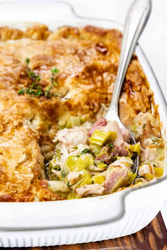 a close up image of Turkey and Ham Pie with a serving spoon full of a scoop of turkey, ham and leek filling.