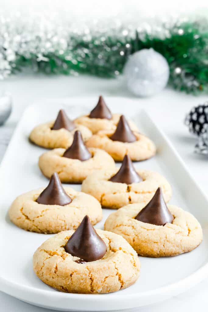 A plate of peanut butter blossom cookies with a festive holiday background.