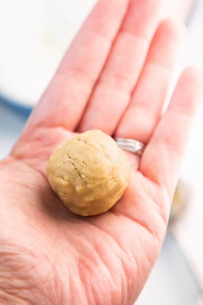 A hand holding a ball of peanut butter cookie dough.