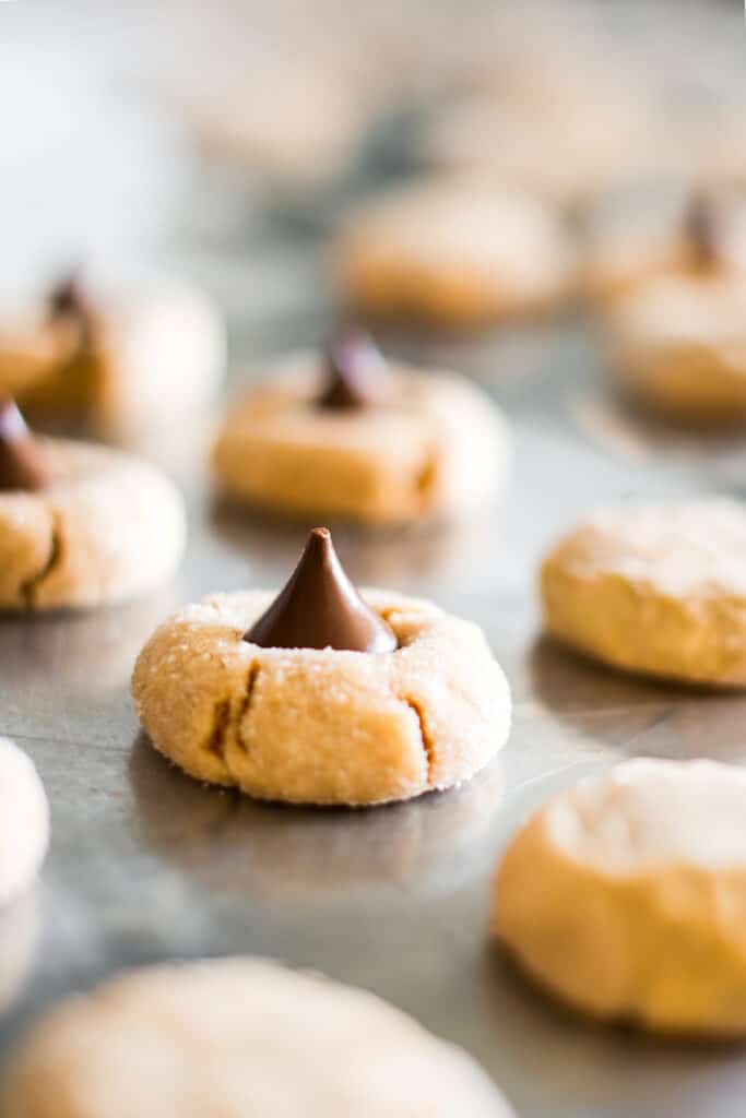 Close-up of a peanut butter blossom cookie with a chocolate kiss on a baking sheet.