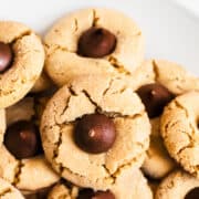 A close up image of a plate of peanut butter blossom cookies with chocolate kisses in the center.