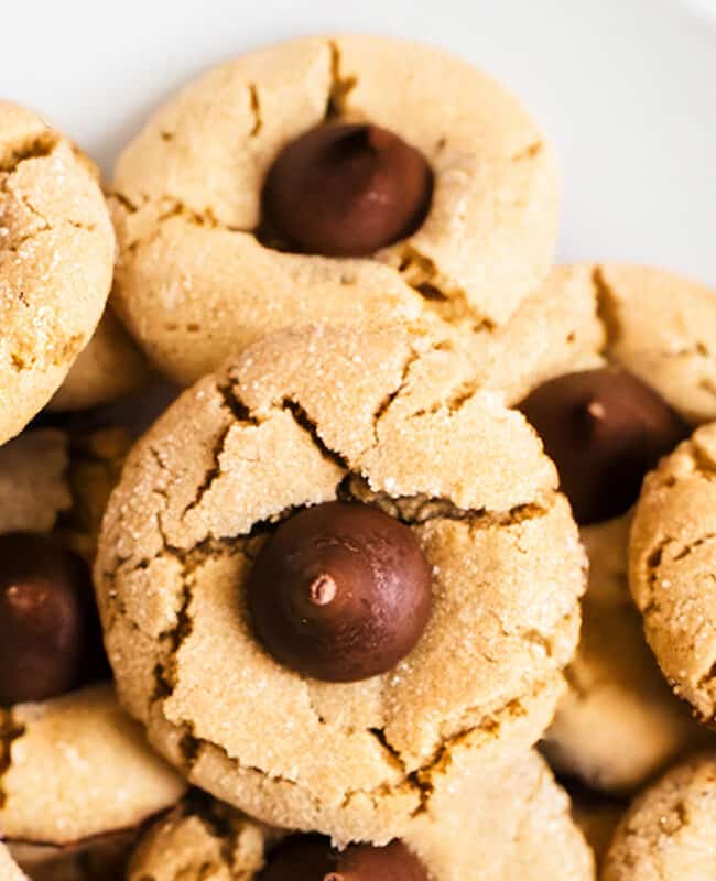 A close up image of a plate of peanut butter blossom cookies with chocolate kisses in the center.