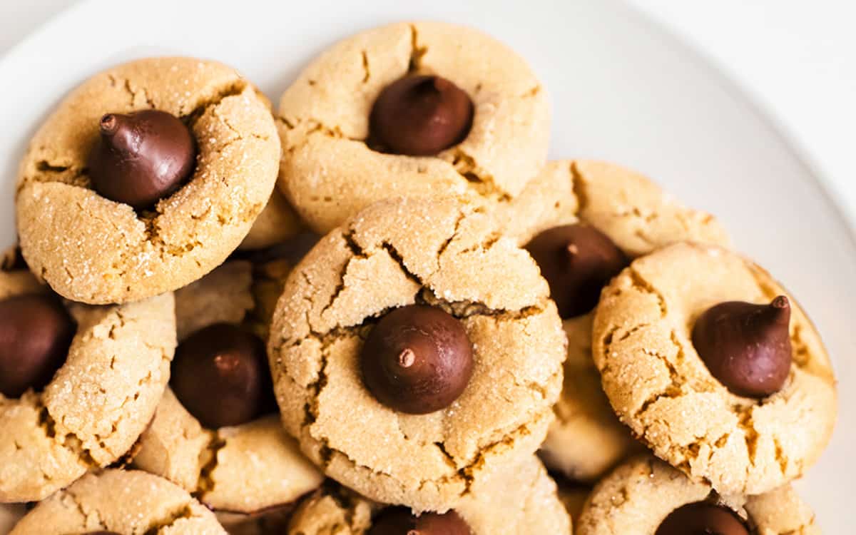 A close up image of a plate of peanut butter blossom cookies with chocolate kisses in the center.