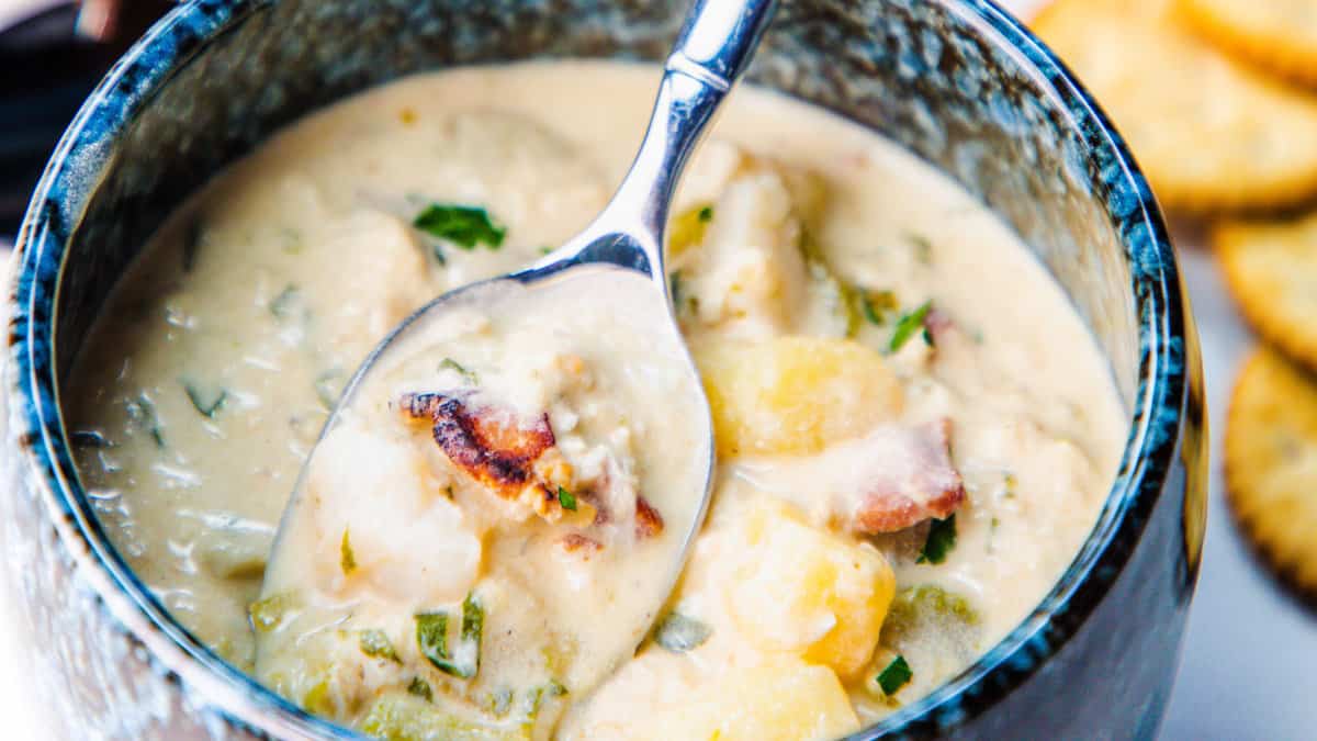 A bowl of creamy crab soup with chunks of crab meat and slices of potato, garnished with fresh herbs, served with crackers on the side.