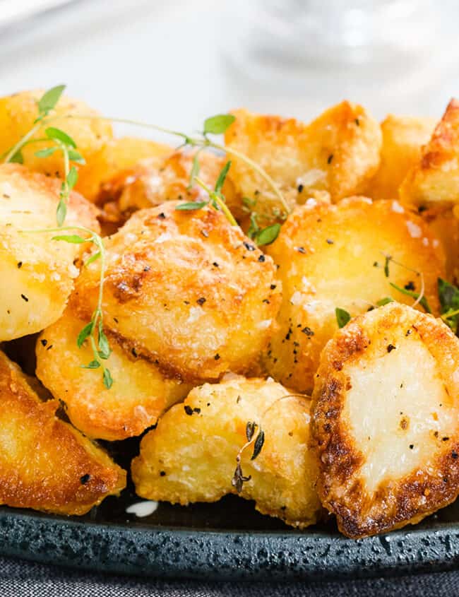 a close up image of a plate piled high with crispy roasted potatoes garnished with fresh thyme.