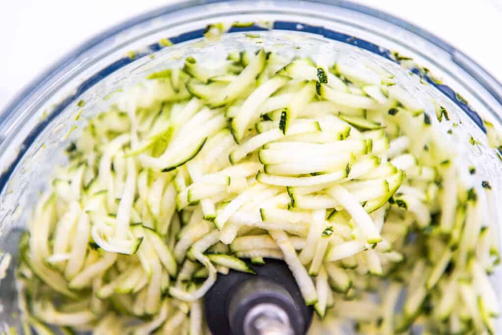 Freshly shredded zucchini displayed inside a food processor bowl, ready for use in recipes.