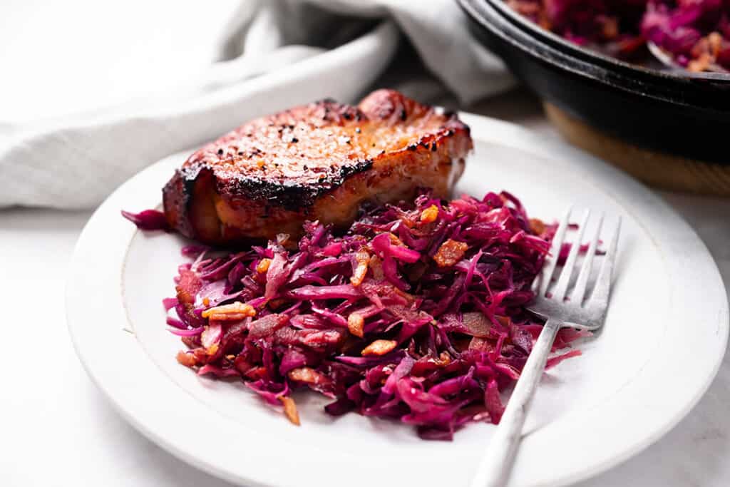 A white plate with braised purple cabbage and a seared pork chop.