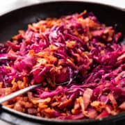 a close up image of braised Purple cabbage scattered with crispy bacon in a cast iron pot.