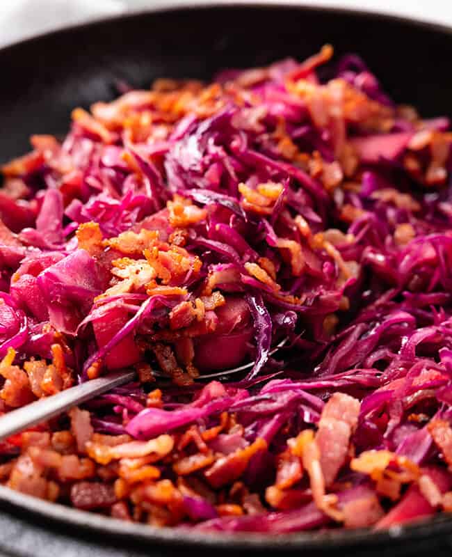 a close up image of braised Purple cabbage scattered with crispy bacon in a cast iron pot.