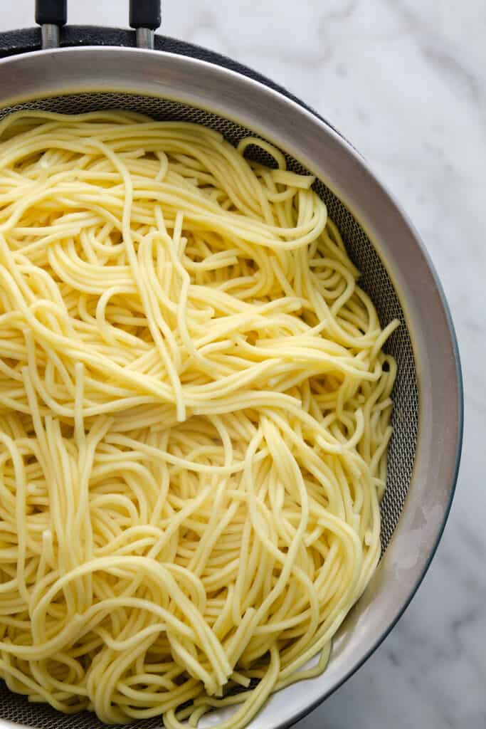 A strainer full of cooked yellow noodles on a marble surface.