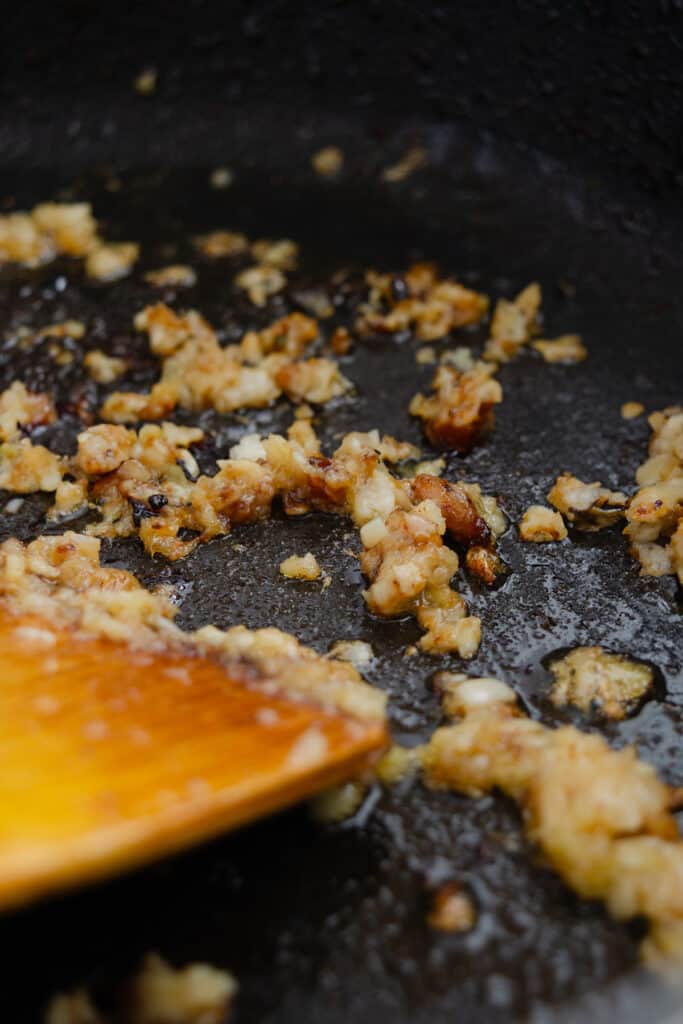 Crispy bits of fried ginger and garlic in a skillet with a wooden spatula.