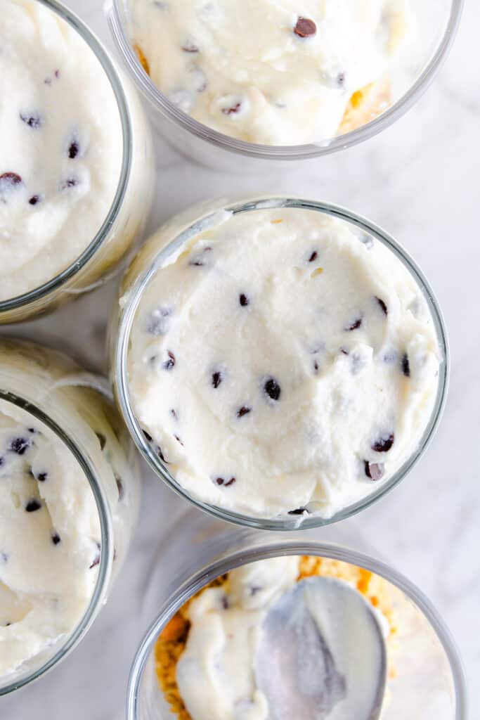 Overhead view of several glasses filled with creamy ricotta dessert, dotted with chocolate chips, ready to be served.