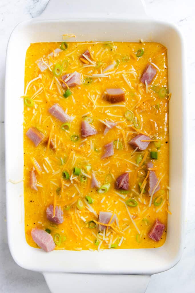 Unbaked ham and cheese casserole mixture with green onions in a white baking dish, ready to be cooked.