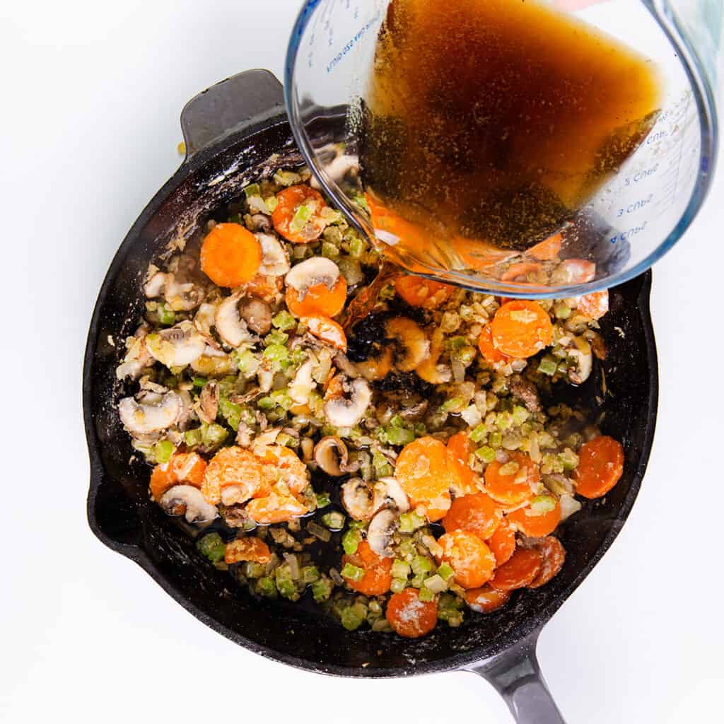 Beef stock being poured over the flour coated vegetables in the pan.