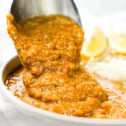 A spoonful of red lentil dal being served onto rice.
