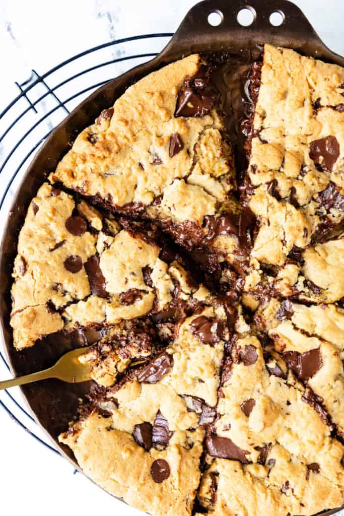 Overhead view of a golden-brown Pizookie with rich chocolate chunks, some melting, showing a slice being lifted by a gold fork.