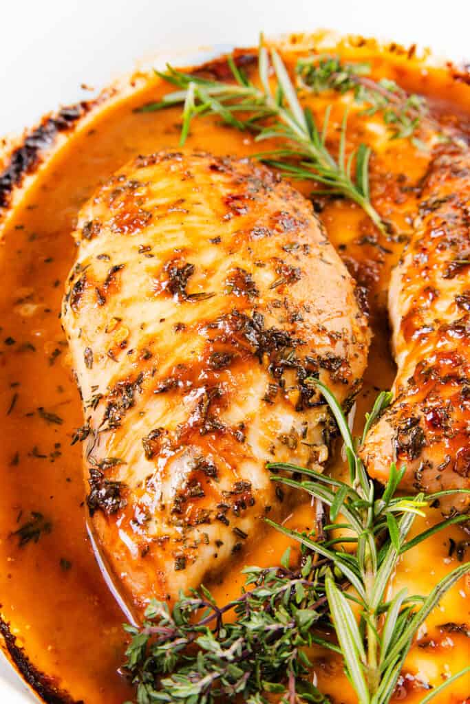 The image shows a close-up of a turkey tenderloin with a beautifully browned and seasoned crust, basking in a pool of what appears to be a savory sauce. Fresh rosemary is placed around the tenderloin, which adds to the dish's aromatic appeal.