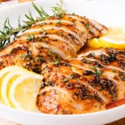 The image shows a succulent turkey tenderloin that has been cooked and sliced, garnished with rosemary and lemon slices, and served with a glistening sauce.