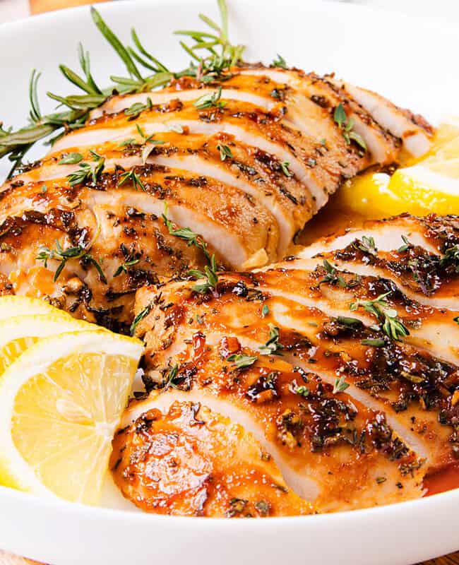 The image shows a succulent turkey tenderloin that has been cooked and sliced, garnished with rosemary and lemon slices, and served with a glistening sauce.