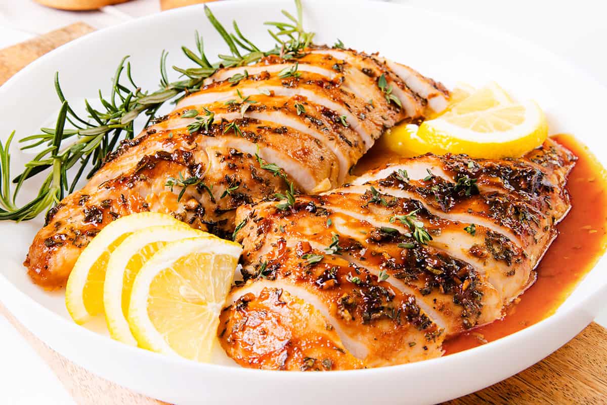 The image shows a succulent turkey tenderloin that has been cooked and sliced, garnished with rosemary and lemon slices, and served with a glistening sauce.