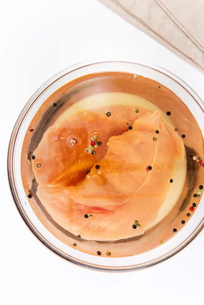 The image shows a raw turkey tenderloin soaking in a brine solution. You can see colorful peppercorns floating in the liquid.