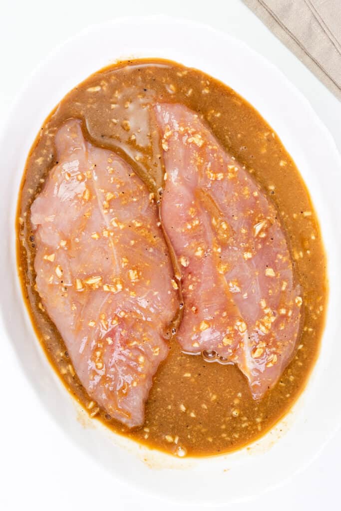 two turkey tenderloins marinading in a white bowl.