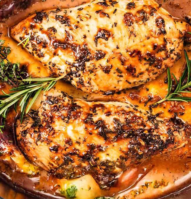 Close-up of turkey tenderloin and seasoned chicken breasts cooked in a slow cooker with herbs, rosemary, and vegetables in a savory sauce.