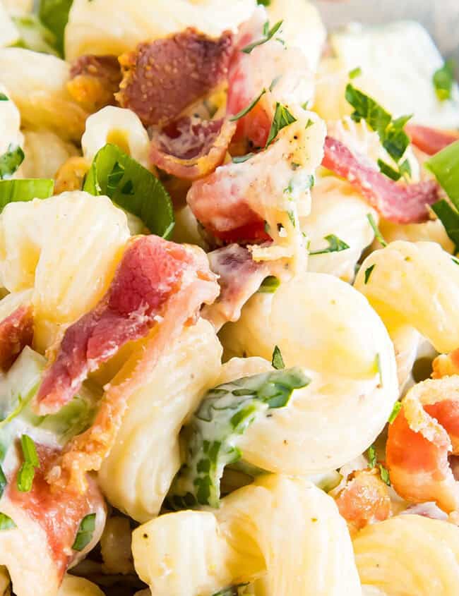 A close up image of pasta salad with bacon and green onions in a bowl.